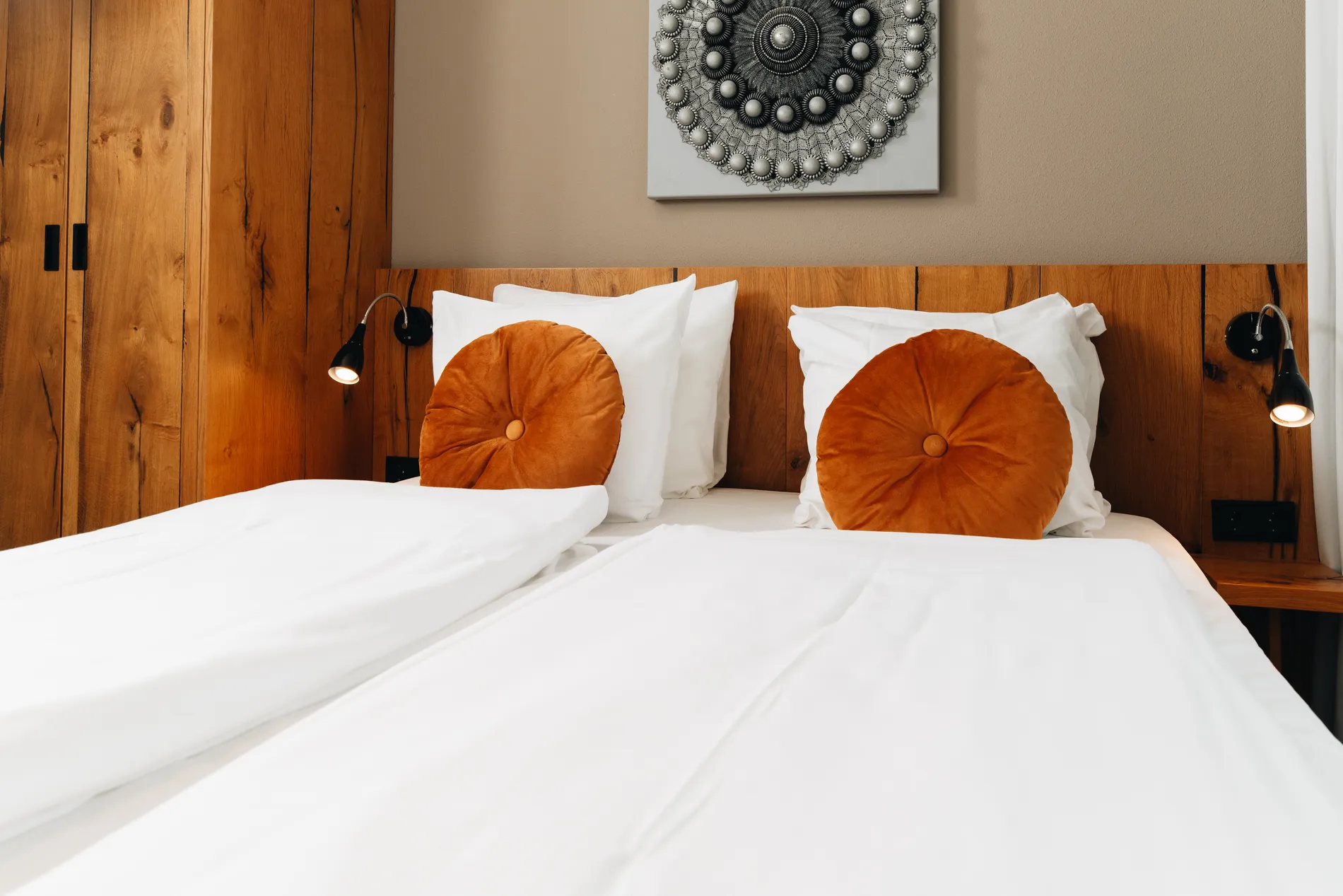 Luxe hotelkamer bij Resort Land & Zee met een opgemaakt tweepersoonsbed, opvallende oranje ronde sierkussens, een houten hoofdbord en moderne wanddecoratie.